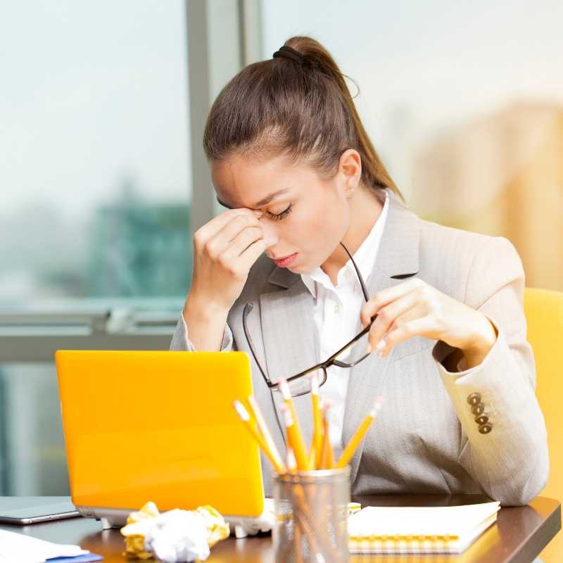 An exhausted professional woman in a business suit sitting at her desk with a laptop.