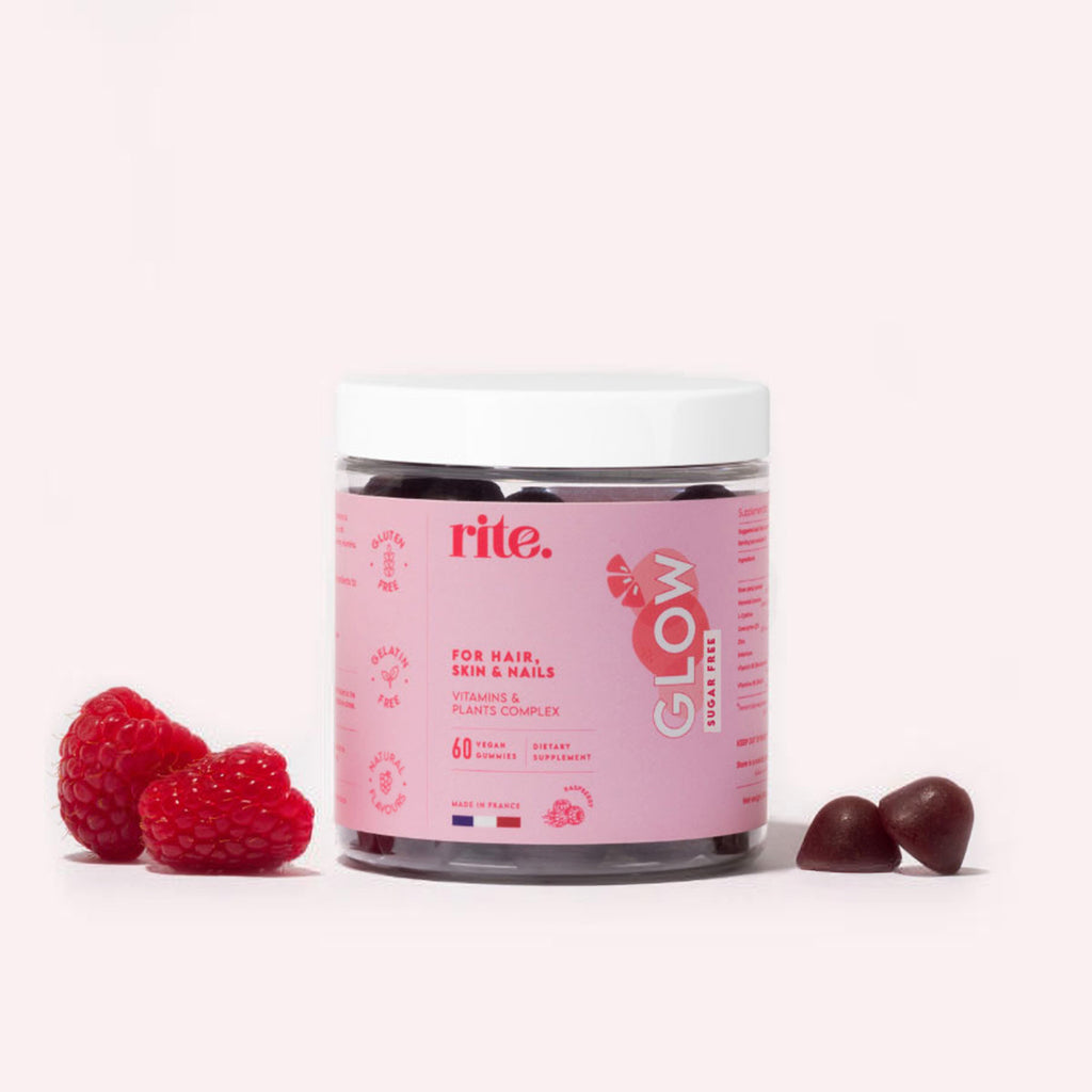 A jar filled with glow gummies sits on a white background next to two raspberries.