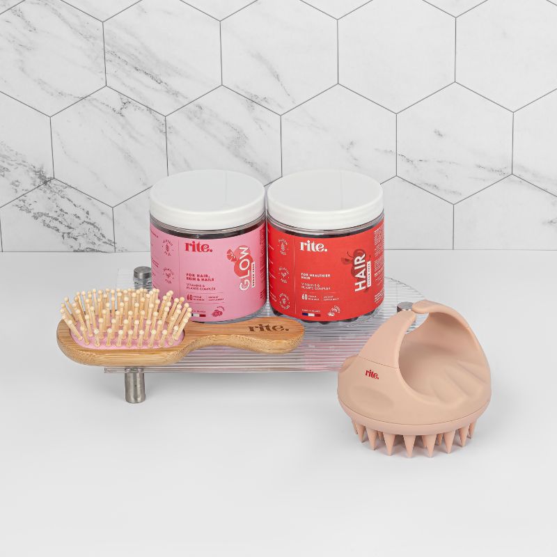 A bathroom shelf with a hair brush, two jars of GLOW and HAIR gummies, and a scalp massage. 