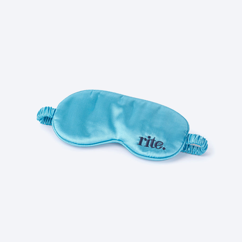 A blue sleep mask with the word "Rite" embroidered on the front in white thread.