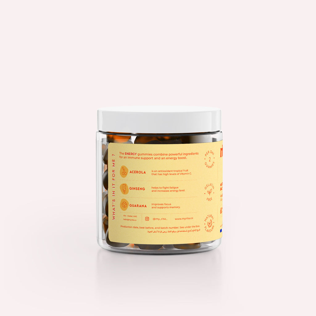 A jar of Rite ENERGY Vegan Gummies sits on a surface next to an orange slice and a single gummy bear. 