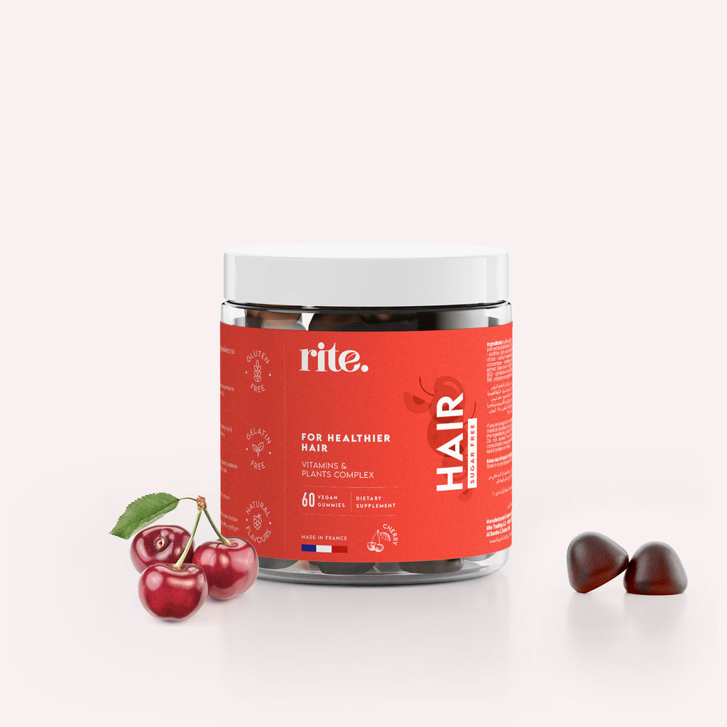 A jar of “rite for healthier hair vitamins & plants complex 60 dietary hair sugar free” gummies sits on a table next to a  red cherry.