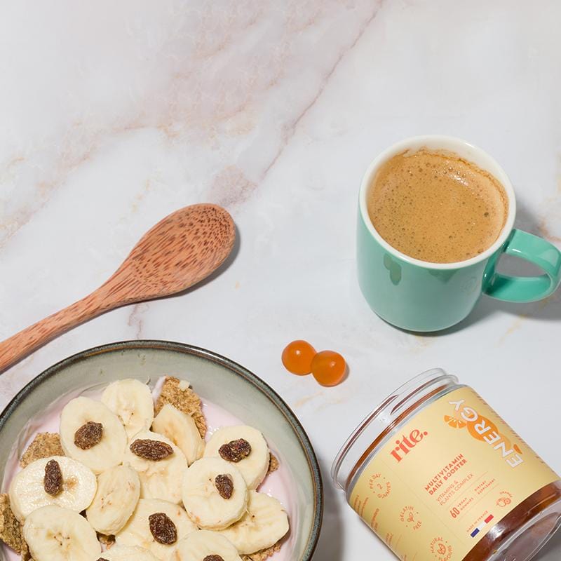 Bowl of cereal with banana slices and raisins next to a cup of coffee and a jar of Rite Energy Vegan Gummies.